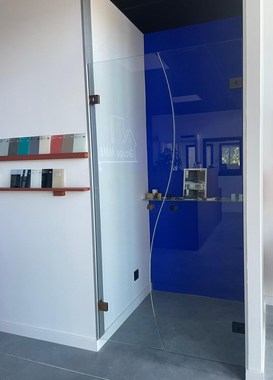 Showroom du Groupe MMB : porte en verre gravée, échantillons de vitrages AGC et poignées exposés